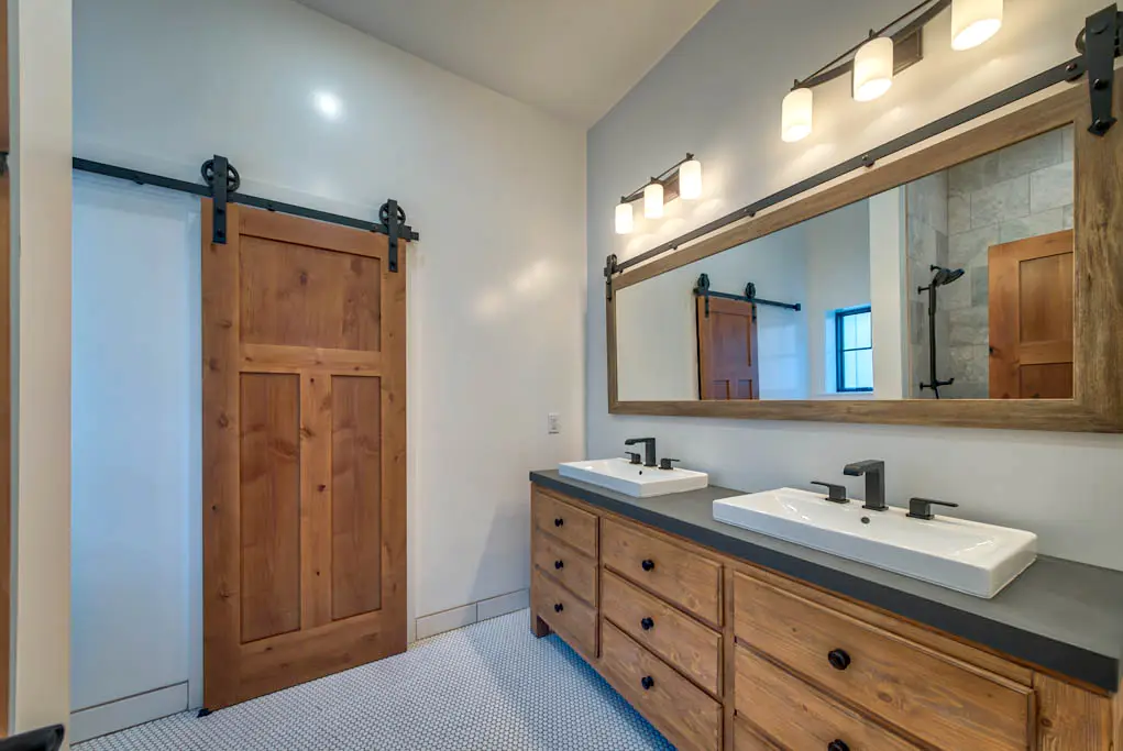 Interior photo of custom-built home by Harvell Homes in Powell, Wyoming featuring a luxurious bathroom with double sinks, a sliding barn door, and a floor-to-ceiling tile walk-in shower
