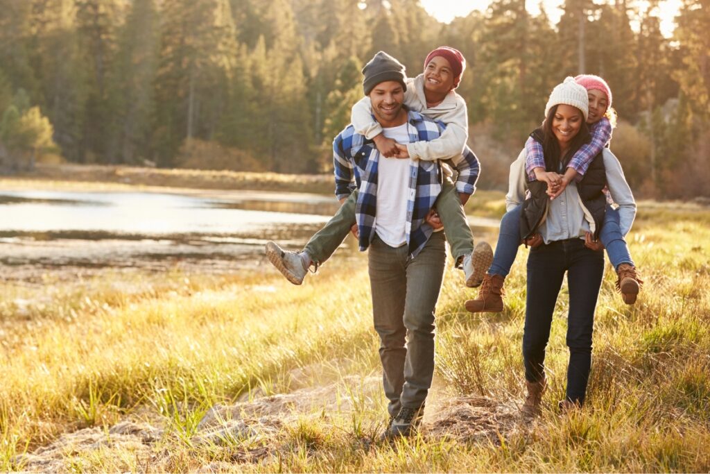 Image of parents with kids on each of their backs strolling through a park